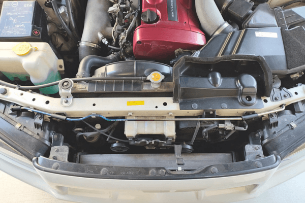 Engine bay view of Skyline BNR34 with FUJITSUBO EXH+ Hood Support mounted, highlighting titanium rod placement and compatibility.